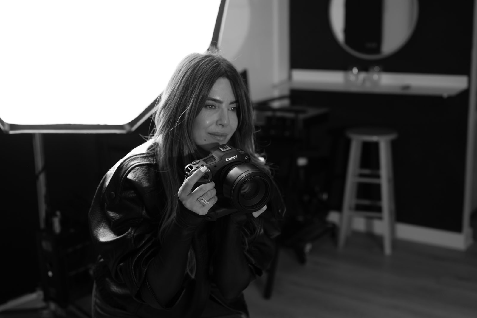Shiran at work in her studio, holding her camera up to photograph, in black and white.