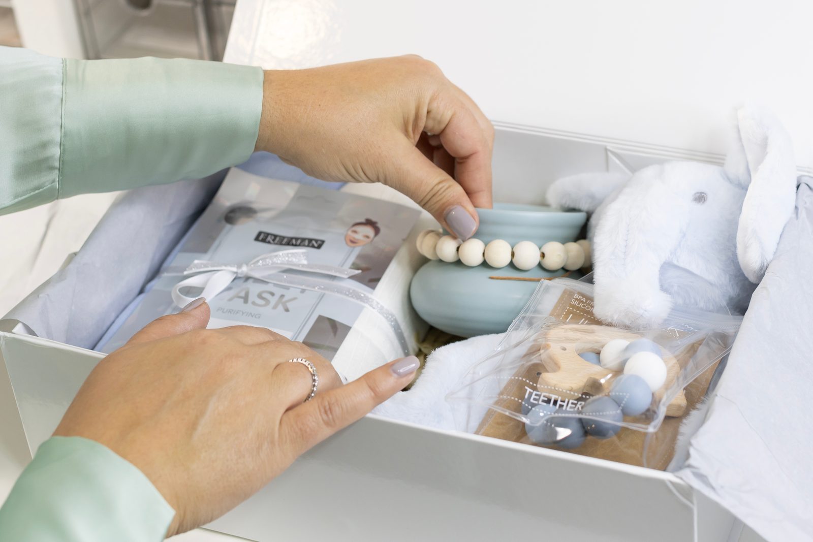 Hands arrange small items in a white gift box lined with tissue.