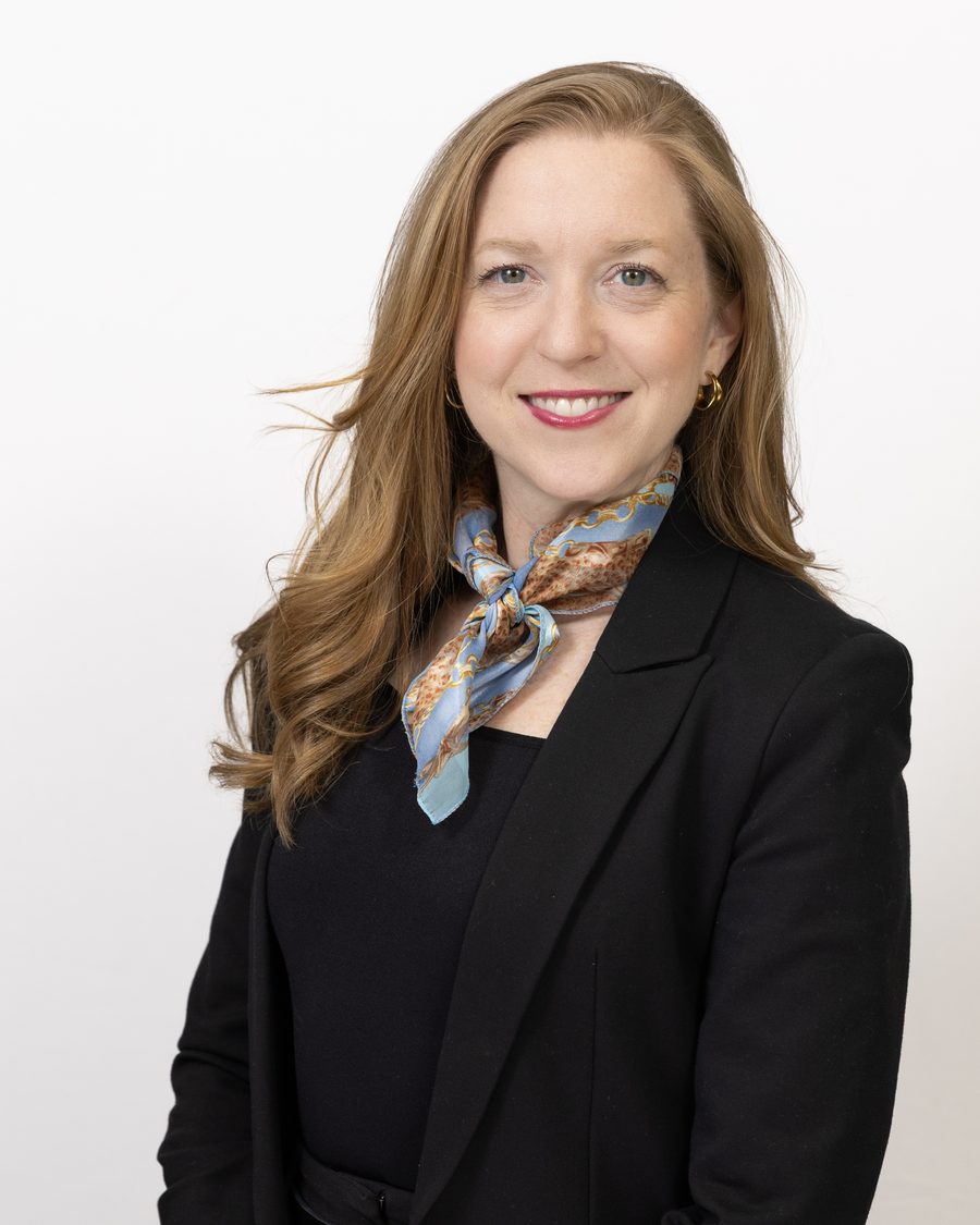Corporate headshot of a professional wearing a patterned scarf and black blazer on a white studio background.